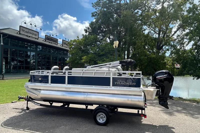 Slide: The Image of 2026 Sun Tracker Bass Buggy 18 DLX pontoon boat on trailer near a lake. - 3
