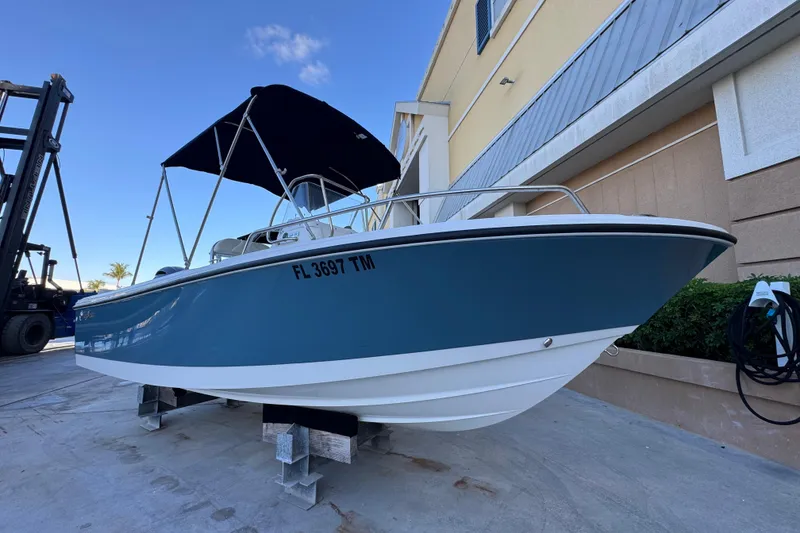 Slide: The Image of 2023 Edgewater 188CC boat with blue hull and black canopy, docked outdoors. - 1