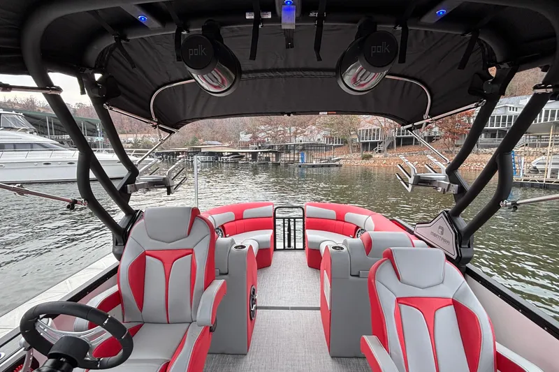 Slide: The Image of 2025 Montara 25 Surf Boss boat interior with red and gray seating, docked by the water. - 22