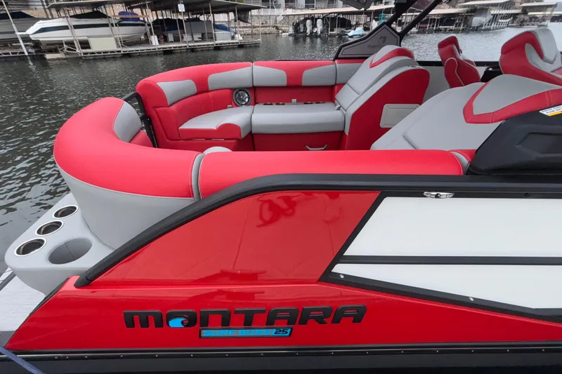 Slide: The Image of 2025 Montara 25 Surf Boss boat with red and gray seating, docked by the water. - 50
