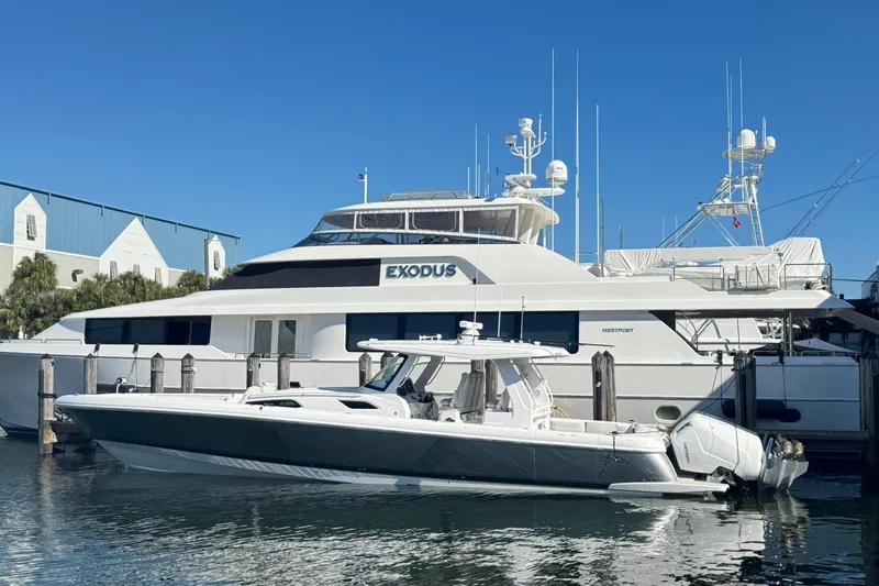 The Image of 2025 Intrepid 51 Panacea yacht docked beside a larger vessel, under clear blue skies. - 1