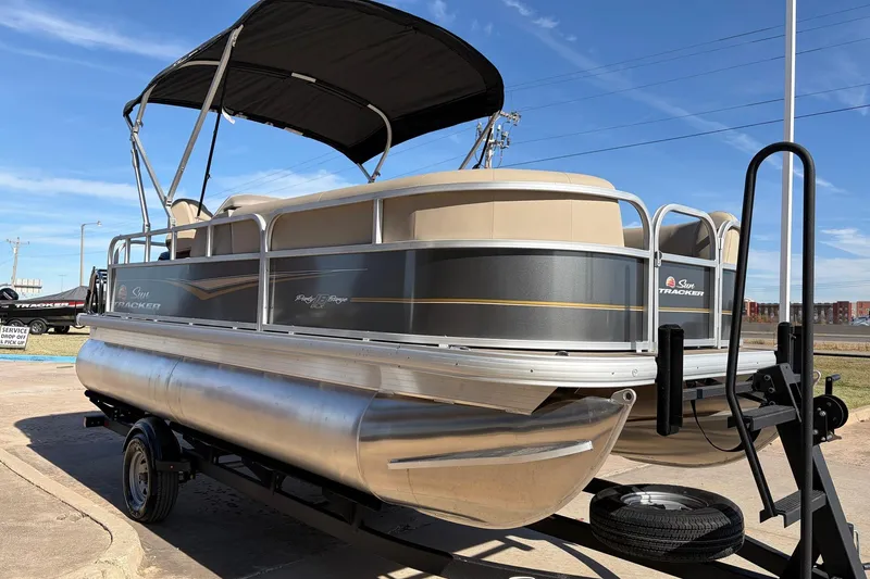 Slide: The Image of 2024 Sun Tracker Party Barge 18 DLX pontoon boat on trailer, under clear blue sky. - 4