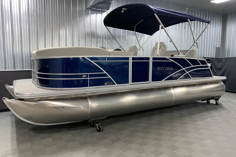 Slide: The Image of 2026 Sylvan Mirage 8522 CLZ DH pontoon boat in showroom, blue and silver design. - 13
