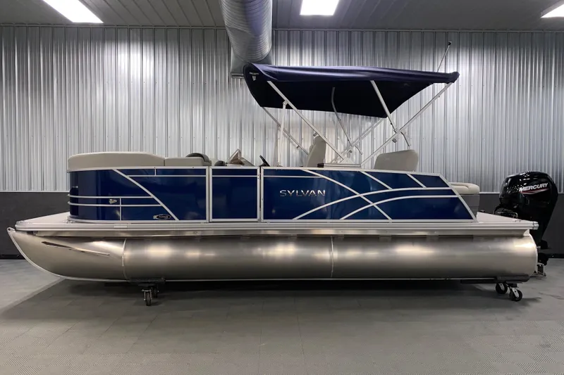 Slide: The Image of 2026 Sylvan Mirage 8522 CLZ DH pontoon boat in showroom, blue and silver design. - 16