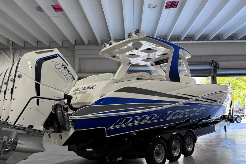 Slide: The Image of 2024 Deep Impact 399 Sport boat on trailer, white and blue design, parked outdoors. - 4