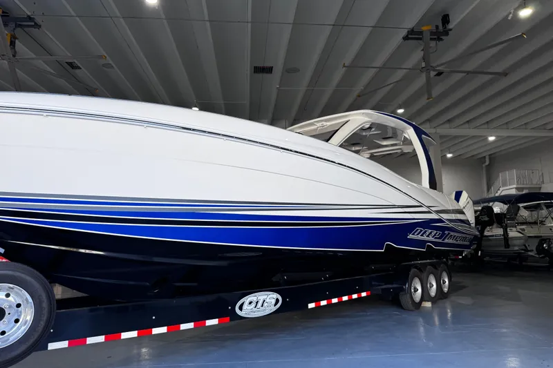 Slide: The Image of 2024 Deep Impact 399 Sport boat on trailer, blue and white design, parked outdoors. - 7