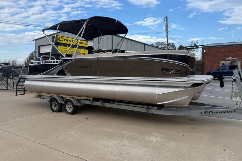 The Image of 2026 Avalon LSZ Versatile Rear Bench pontoon boat on trailer, parked outdoors. - 0