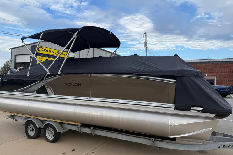 Slide: The Image of 2026 Avalon LSZ Versatile Rear Bench pontoon boat on trailer, covered, outside dealership. - 7