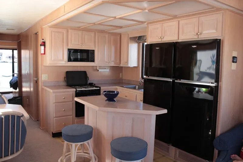Slide: The Image of 1996 Stardust Cruisers 1655 houseboat kitchen with wooden cabinets and black appliances. - 12