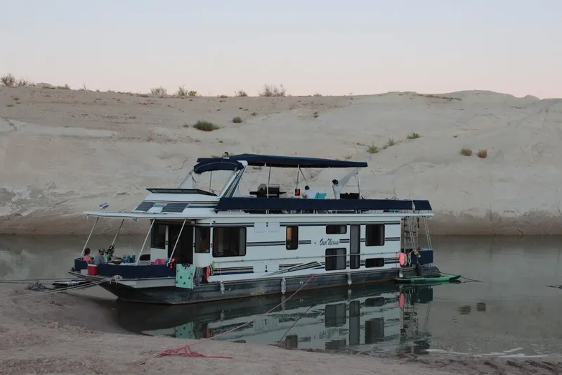 Slide: The Image of 1996 Stardust Cruisers 1655 houseboat moored on a calm riverbank, surrounded by sandy terrain. - 3