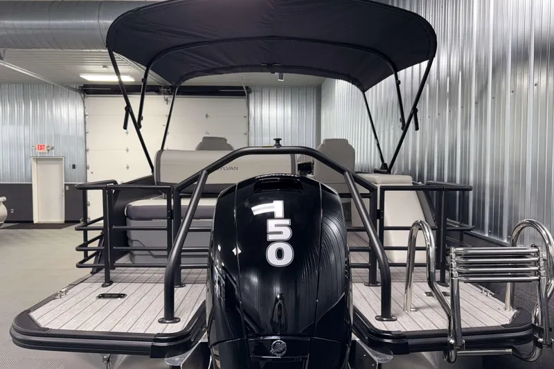 Slide: The Image of 2026 Sylvan Mirage X1 pontoon boat with a 50 HP engine in a metal-walled showroom. - 24