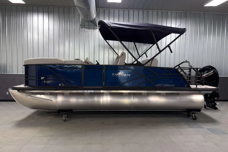 Slide: The Image of 2026 Sylvan MIRAGE X1 CLZ DH pontoon boat with blue exterior and canopy in showroom. - 19