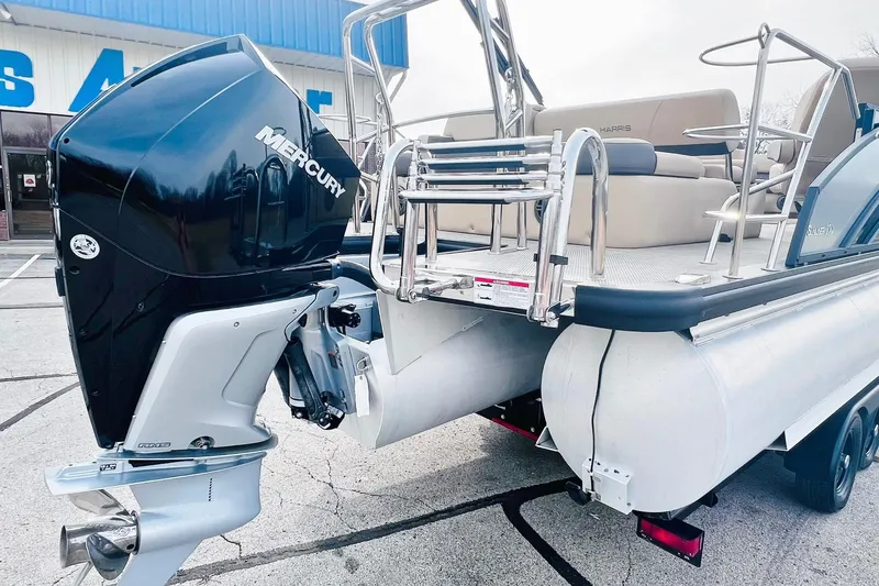 Slide: The Image of 2024 Harris Sunliner 250 pontoon boat with Mercury outboard engine, parked on a trailer. - 7