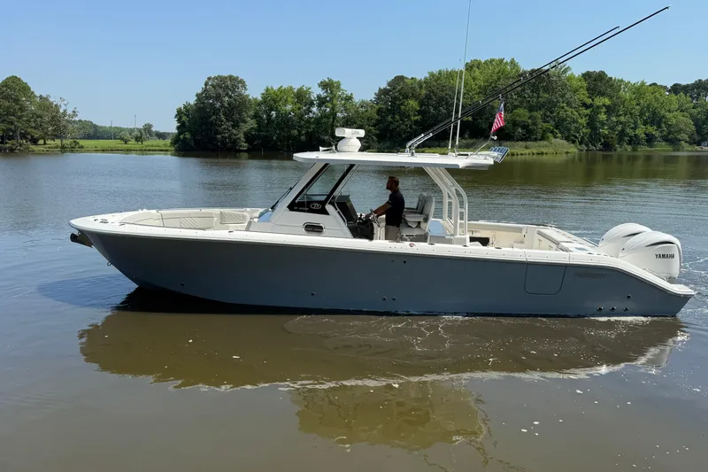 Slide: The Image of 2024 Pursuit S 328 Sport boat cruising on a calm lake with lush green trees. - 14