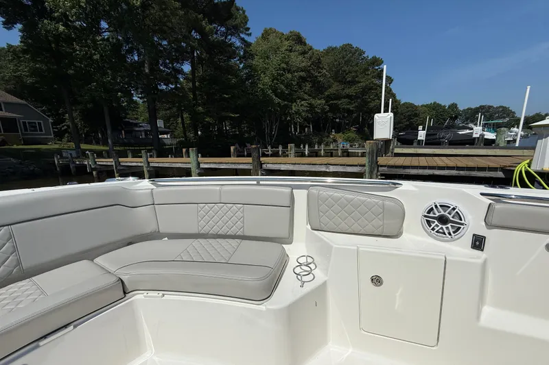 Slide: The Image of 2024 Pursuit S 328 Sport boat interior with cushioned seating and speaker, docked by trees. - 17