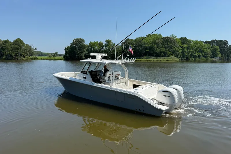 Slide: The Image of 2024 Pursuit S 328 Sport boat cruising on a calm lake with lush green trees. - 2
