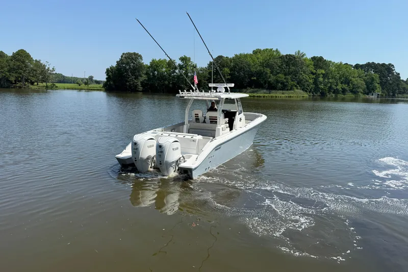 Slide: The Image of 2024 Pursuit S 328 Sport boat cruising on a calm lake with lush green trees. - 5