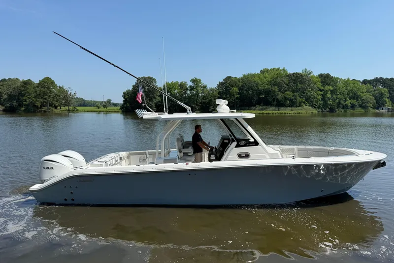 Slide: The Image of 2024 Pursuit S 328 Sport boat cruising on a calm lake with lush green shoreline. - 8