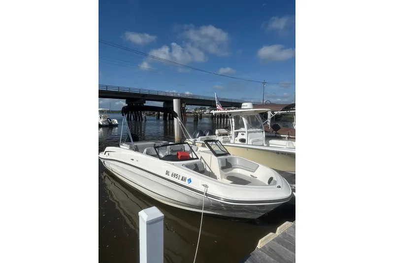 The Image of 2022 Bayliner VR6 Bowrider OB docked by a bridge under a clear blue sky. - 0