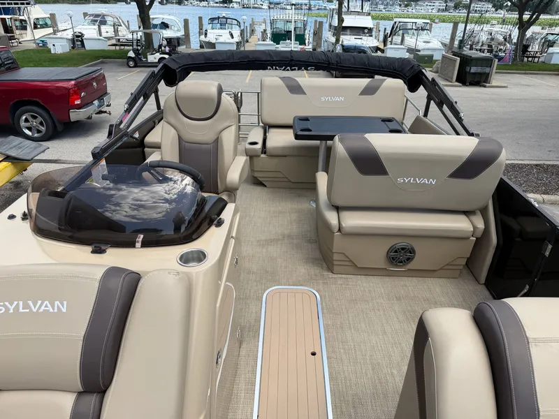 Slide: The Image of The image shows the interior of a 2022 Sylvan L1 DLZTT pontoon boat. It features beige upholstery and a table. - 13