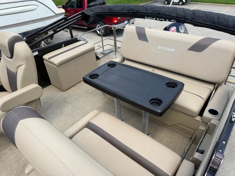 Slide: The Image of The image shows the interior of a 2022 Sylvan L1 DLZTT pontoon boat with beige seating and a table. - 27