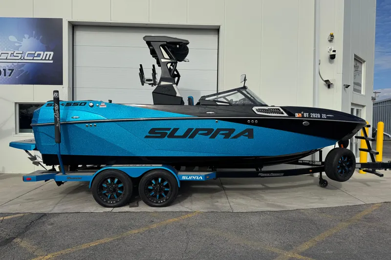 The Image of 2021 Supra SA 575 boat in vibrant blue, parked on a trailer outside a building. - 0