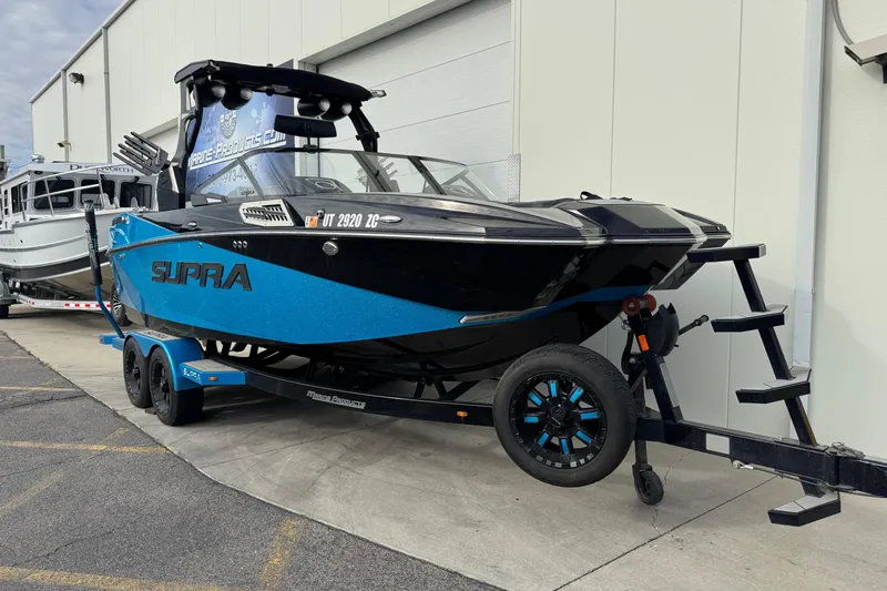 Slide: The Image of 2021 Supra SA 575 boat in blue and black on a trailer, parked outdoors. - 3