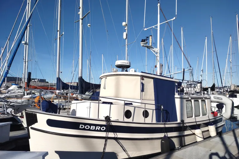 The Image of 1990 Nordic Tug 32 docked at marina, surrounded by sailboats under clear blue sky. - 0