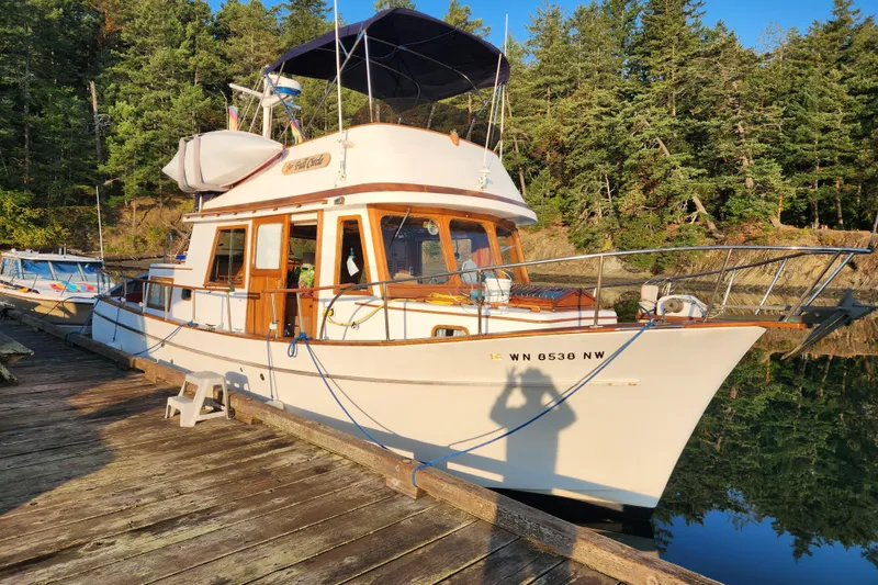 The Image of 1976 CHB Double Cabin Trawler docked by a forested shoreline. - 0