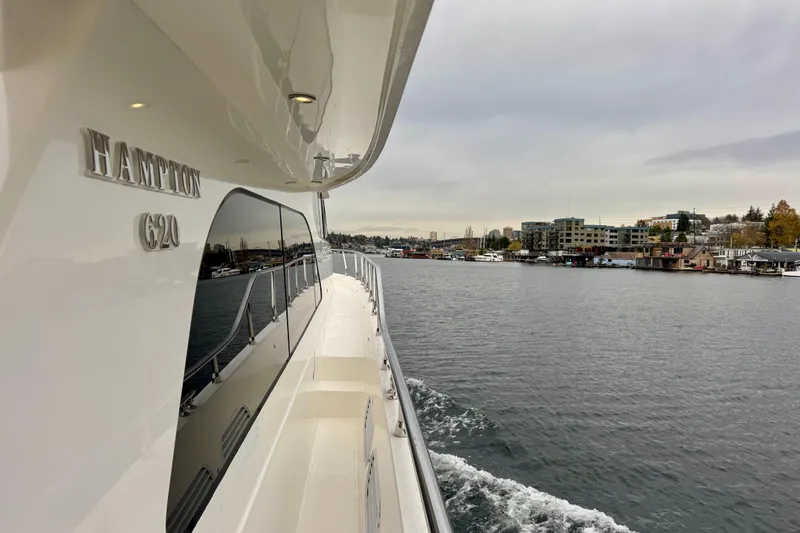 Slide: The Image of 2013 Hampton 620 Pilothouse yacht cruising near waterfront buildings under cloudy skies. - 5