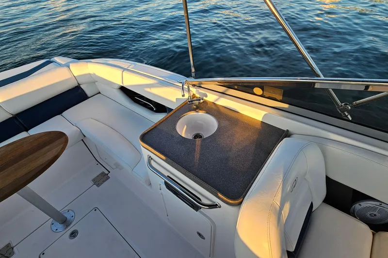 Slide: The Image of 2008 Regal 2700 ES Bowrider interior with sink, seating, and table on calm water. - 24