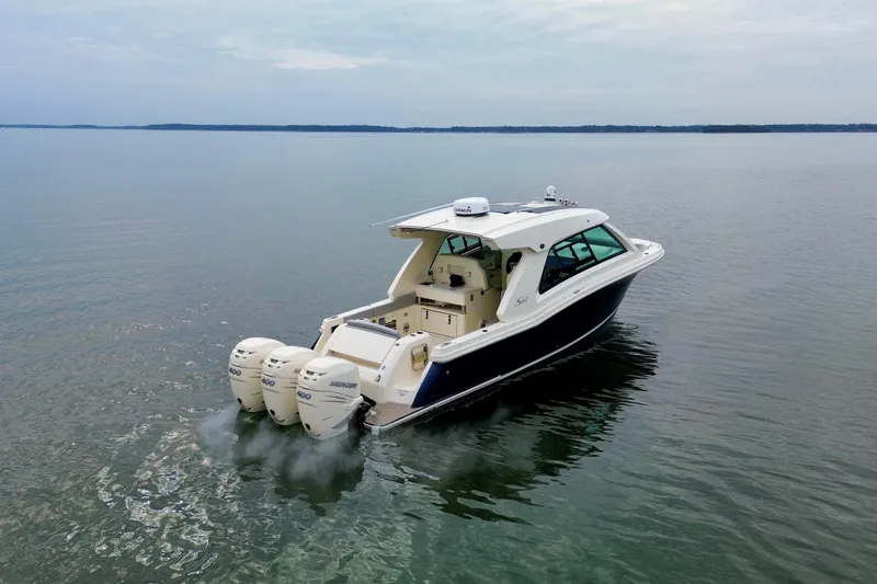 Slide: The Image of 2023 Scout 350 LXZ boat cruising on calm waters with triple Mercury engines. - 12