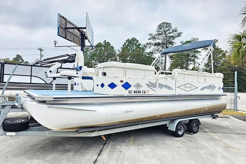 Slide: The Image of 2004 Bentley Pontoons 240 Fish on trailer, featuring blue accents and canopy, parked outdoors. - 1