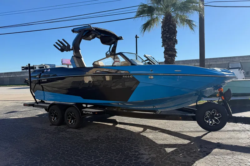 The Image of 2026 Supra SL 550 boat on trailer, blue and black design, parked outdoors. - 1