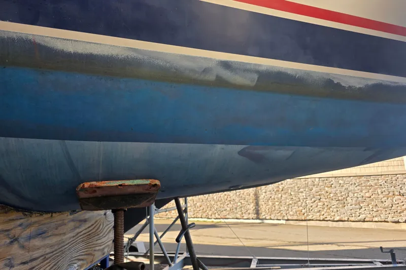 Slide: The Image of 1985 Express Yachting Express 30 sailboat hull on dry dock, showing blue and red stripes. - 29