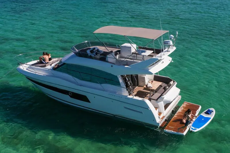 Slide: The Image of 2020 Prestige 460 yacht on clear turquoise water, featuring a spacious deck and sunbathing area. - 5