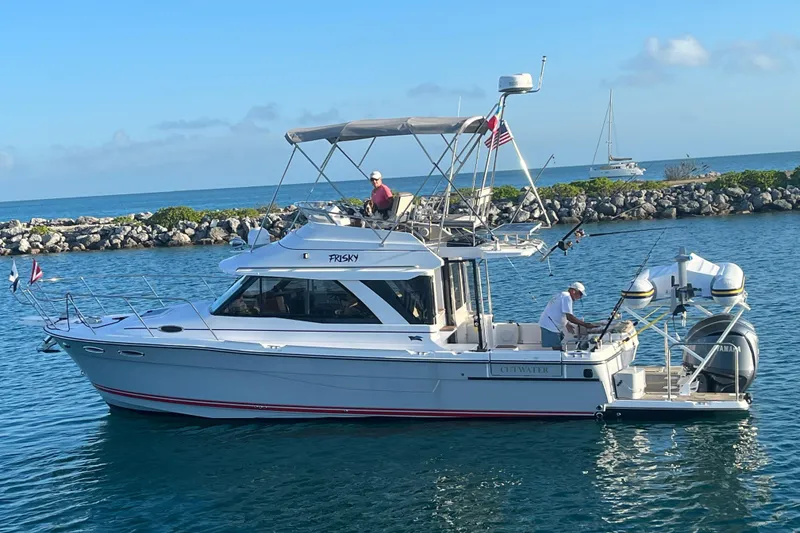The Image of 2022 Cuwater C-32-CB boat cruising in clear blue waters near rocky shoreline. - 0