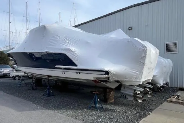 Slide: The Image of Covered 2022 Tiara Yachts 43 LS in storage, supported by stands, near a warehouse. - 2