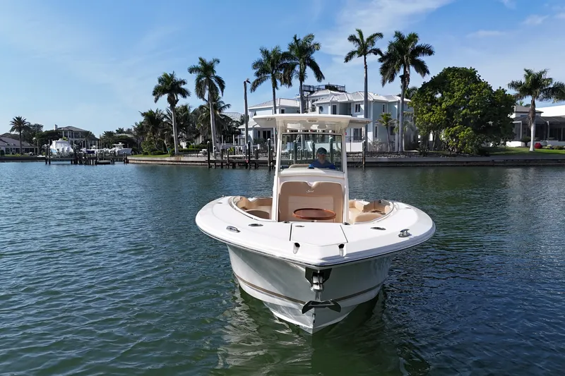 Slide: The Image of 2019 Scout 275 LXF boat on calm water with palm trees and houses in the background. - 2