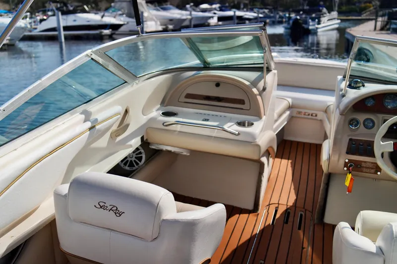 Slide: The Image of 1995 Sea Ray 200 Bow Rider interior with beige seating and wooden flooring at a marina. - 21