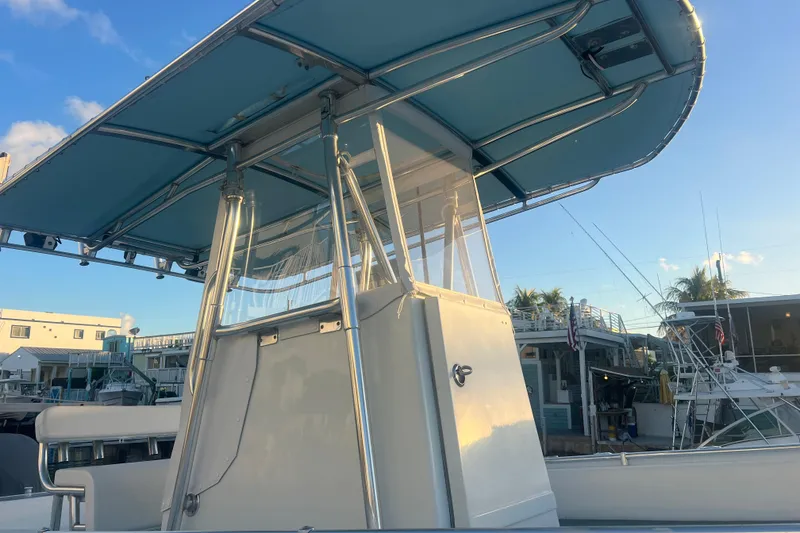 Slide: The Image of 2003 Contender 27 Open boat with blue canopy, docked under clear sky. - 60