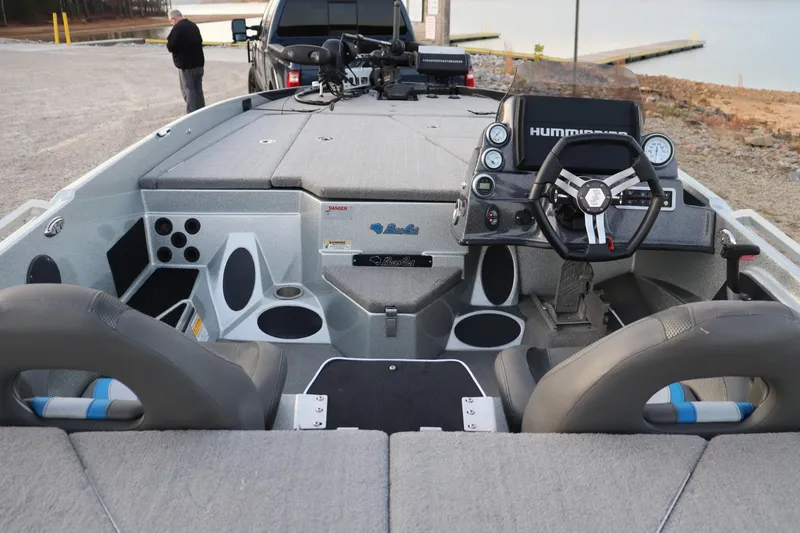 Slide: The Image of 2019 Bass Cat Lynx boat interior with steering wheel and seating, parked near a lake. - 17