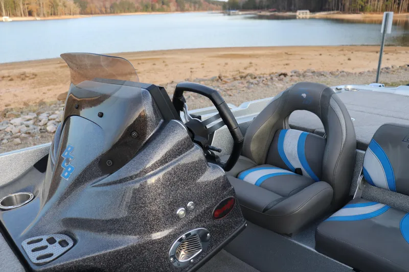 Slide: The Image of 2019 Bass Cat Lynx boat interior with steering wheel and blue-accented seats by a lake. - 8