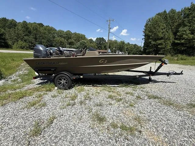 The Image of 2023 G3 Gator Tough 17 SC boat on trailer, parked on gravel with trees in background. - 1