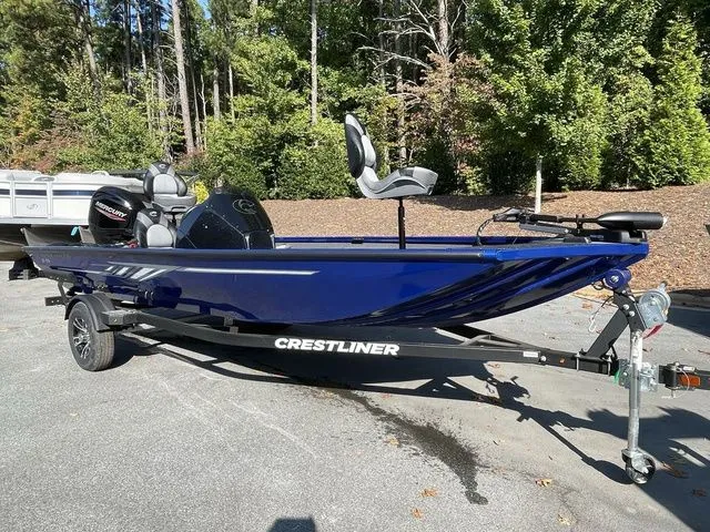 Slide: The Image of 2023 Crestliner XFC 179 boat on trailer, parked outdoors, surrounded by trees. - 2