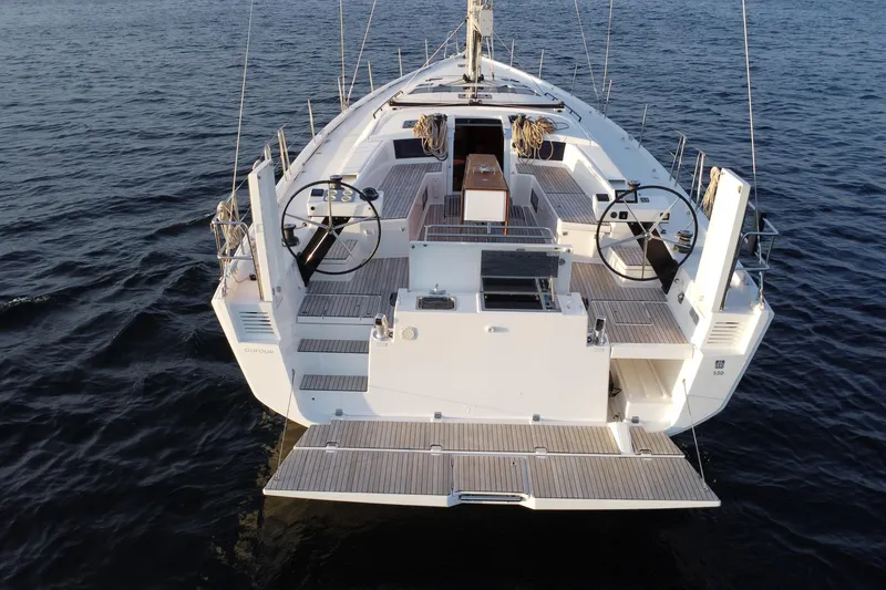 Slide: The Image of 2024 Dufour 530 yacht on calm waters, showcasing spacious deck and dual steering wheels. - 3