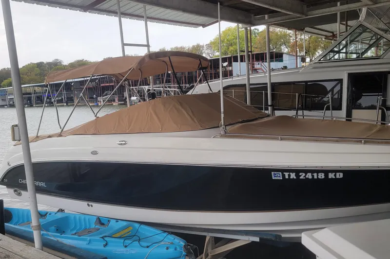 Slide: The Image of 2005 Chaparral 256 SSi boat docked with tan cover and blue kayaks nearby. - 2