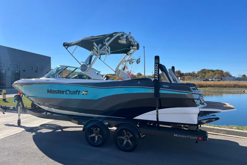 Slide: The Image of 2020 MasterCraft XT23 boat on trailer by a lake under clear blue sky. - 2