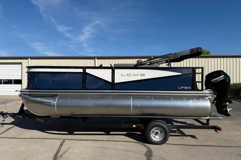 Slide: The Image of 2025 Lowe LF 194 pontoon boat on trailer, parked outdoors under clear blue sky. - 4