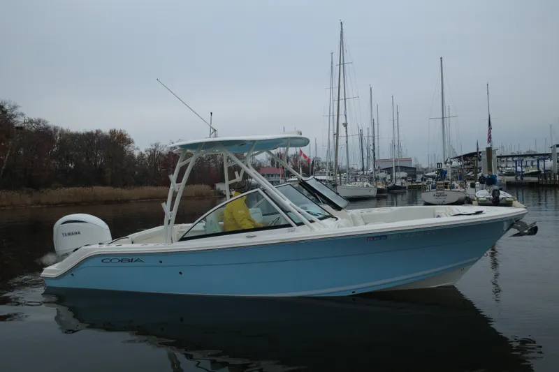 Slide: The Image of 2024 Cobia 240 Dual Console boat on calm water near a marina. - 3